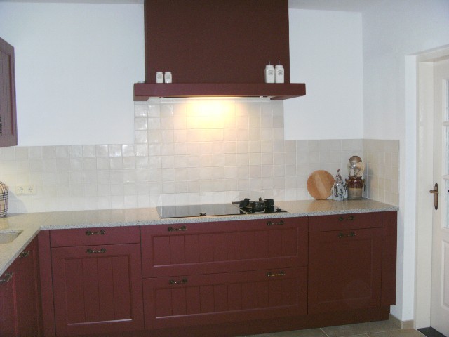 Maatwerk hoek keuken in rood mat lak geplaatst in Arnemuiden. Het aanrechtblad is in Bianco Cristal graniet leather touch uitgevoerd.